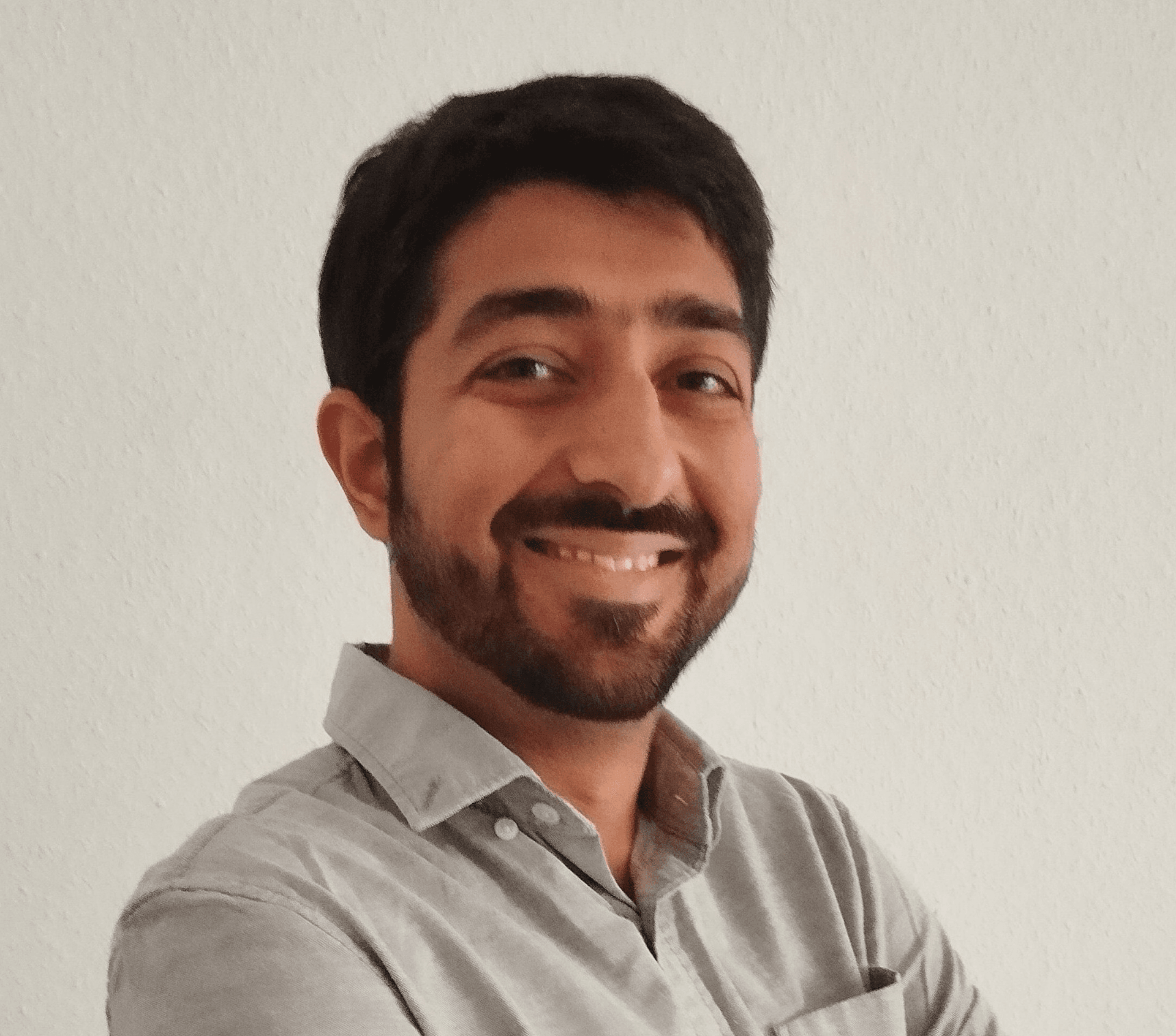 Smiling person with a beard wearing a gray collared shirt against a plain background.